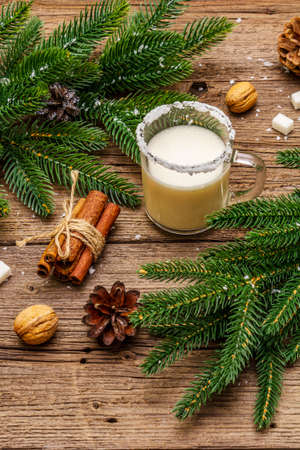 Christmas eggnog liqueur or cola de mono cocktail. Classical winter drink in glass mug, xmas decorations. Evergreen branches, cinnamon, walnuts, sugar. Old wooden backgroundの写真素材