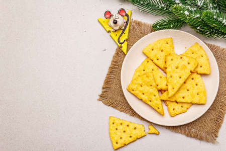 Festive cheese crackers, New Year snack concept. Cookies, mouse figure, fir tree branch, artificial snow, sackcloth napkin. Stone concrete background, copy space, top viewの写真素材