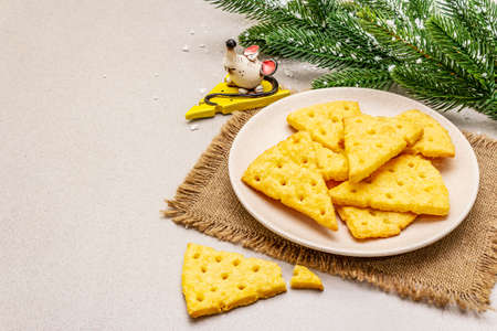 Festive cheese crackers, New Year snack concept. Cookies, mouse figure, fir tree branch, artificial snow, sackcloth napkin. Stone concrete background, copy spaceの写真素材