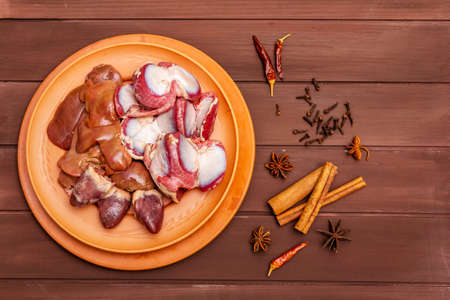 Fresh raw duck offal: heart, liver, stomach. Dry spices: cinnamon, star anise, clove, chili pepper. Wooden boards background, copy space, top viewの写真素材