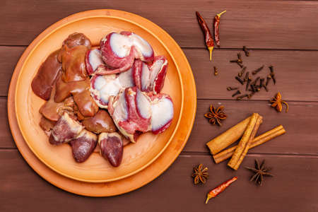 Fresh raw duck offal: heart, liver, stomach. Dry spices: cinnamon, star anise, clove, chili pepper. Wooden boards background, copy space, top view, close upの写真素材