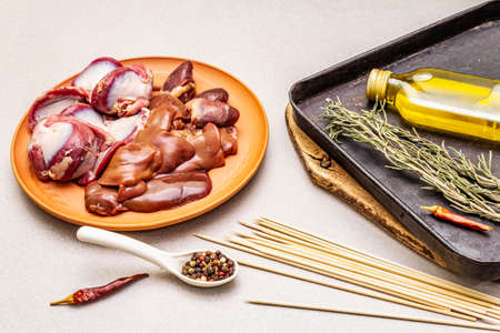 Fresh raw duck offal: heart, liver, stomach. Dry spices, rosemary, chili, oil. Baking tray, wooden skewers, stone concrete backgroundの写真素材