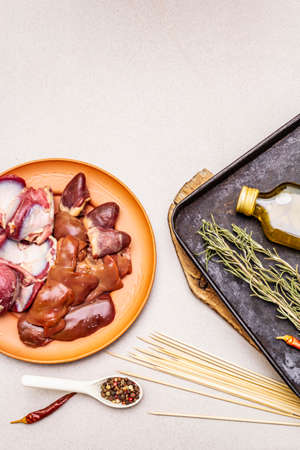Fresh raw duck offal: heart, liver, stomach. Dry spices, rosemary, chili, oil. Baking tray, wooden skewers, stone concrete background, top viewの写真素材
