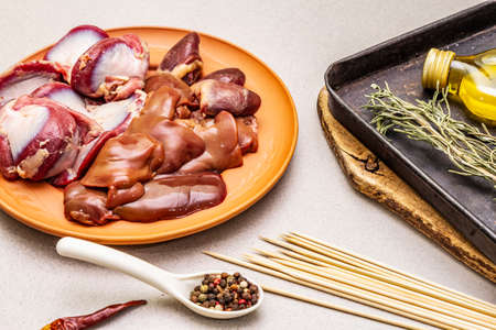 Fresh raw duck offal: heart, liver, stomach. Dry spices, rosemary, chili, oil. Baking tray, wooden skewers, stone concrete background, close upの写真素材