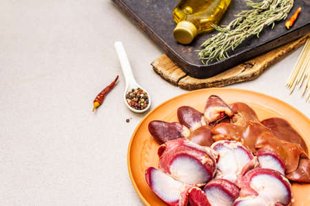 Fresh raw duck offal: heart, liver, stomach. Dry spices, rosemary, chili, oil. Baking tray, wooden skewers, stone concrete background, copy space, close upの写真素材