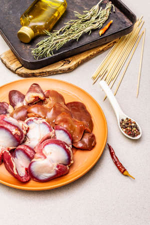 Fresh raw duck offal: heart, liver, stomach. Dry spices, rosemary, chili, oil. Baking tray, wooden skewers, stone concrete background, close upの写真素材