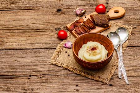Homemade Thanksgiving garlic mashed potatoes with fresh tomatoes and pastrami. Sackcloth napkin, spoons, old wooden boards background, copy spaceの写真素材