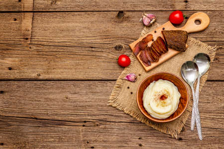 Homemade Thanksgiving garlic mashed potatoes with fresh tomatoes and pastrami. Sackcloth napkin, spoons, old wooden boards background, copy space, top viewの写真素材