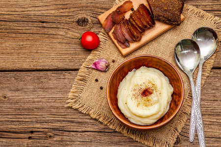 Homemade Thanksgiving garlic mashed potatoes with fresh tomatoes and pastrami. Sackcloth napkin, spoons, old wooden boards background, copy space, top viewの写真素材