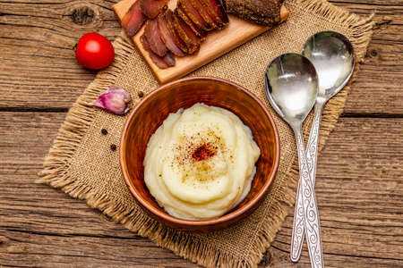 Homemade Thanksgiving garlic mashed potatoes with fresh tomatoes and pastrami. Sackcloth napkin, spoons, old wooden boards background, top view, close upの写真素材