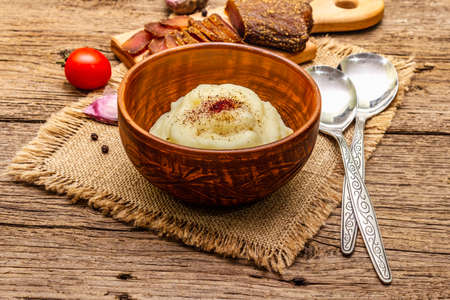 Homemade Thanksgiving garlic mashed potatoes with fresh tomatoes and pastrami. Sackcloth napkin, spoons, old wooden boards background, close upの写真素材