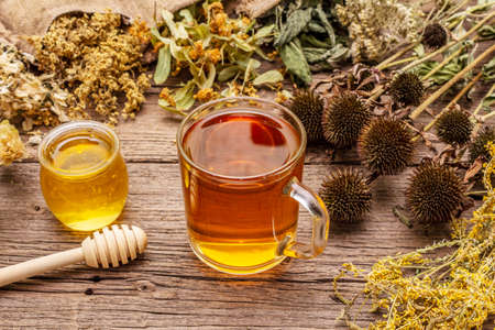 Tea with honey. Herbal harvest collection and bouquets of wild herbs. Alternative medicine. Natural pharmacy, self-care concept. Old wooden boards background, close upの写真素材