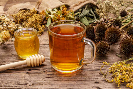 Tea with honey. Herbal harvest collection and bouquets of wild herbs. Alternative medicine. Natural pharmacy, self-care concept. Old wooden boards background, close upの写真素材