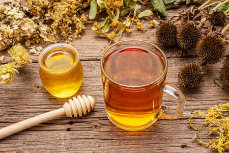Tea with honey. Herbal harvest collection and bouquets of wild herbs. Alternative medicine. Natural pharmacy, self-care concept. Old wooden boards background, close upの写真素材