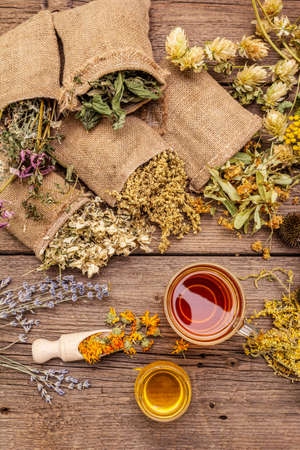 Tea with honey. Herbal harvest collection and bouquets of wild herbs. Alternative medicine. Natural pharmacy, self-care concept. Old wooden boards background, top viewの写真素材