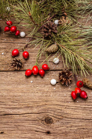 Spirit Christmas background. Fresh dog-rose berries, candies, pine branches and cones, artificial snow. Nature decorations, vintage wooden boards, flat lay, copy spaceの写真素材