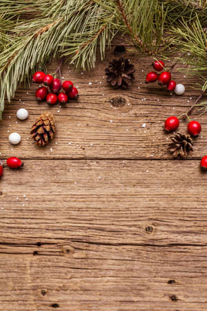 Spirit Christmas background. Fresh dog-rose berries, candies, pine branches and cones, artificial snow. Nature decorations, vintage wooden boards, flat lay, copy spaceの写真素材