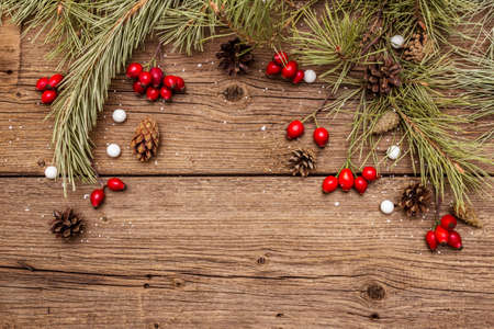 Spirit Christmas background. Fresh dog-rose berries, candies, pine branches and cones, artificial snow. Nature decorations, vintage wooden boards, flat lay, copy space, top viewの写真素材