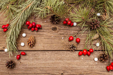 Spirit Christmas background. Fresh dog-rose berries, candies, pine branches and cones, artificial snow. Nature decorations, vintage wooden boards, flat lay, copy space, top viewの写真素材