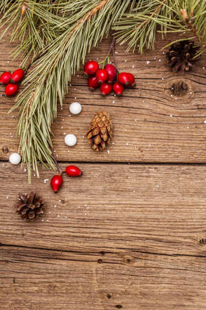 Spirit Christmas background. Fresh dog-rose berries, candies, pine branches and cones, artificial snow. Nature decorations, vintage wooden boards, flat lay, copy space, top viewの写真素材