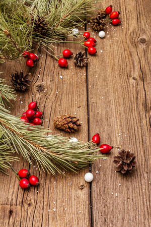 Spirit Christmas background. Fresh dog-rose berries, candies, pine branches and cones, artificial snow. Nature decorations, vintage wooden boards, flat lay, copy space, close upの写真素材