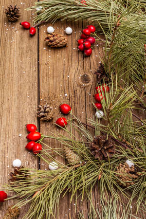Spirit Christmas background. Fresh dog-rose berries, candies, pine branches and cones, artificial snow. Nature decorations, vintage wooden boards, flat lay, copy space, close upの写真素材