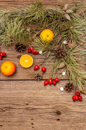Spirit Christmas background. Fresh mandarins, dog-rose berries, candies, pine branches and cones, artificial snow. Nature decorations, vintage wooden boards, flat lay, copy space, top viewの写真素材