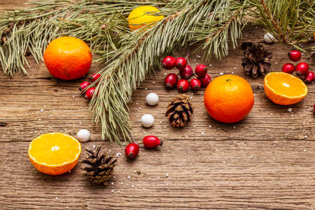 Spirit Christmas background. Fresh mandarins, dog-rose berries, candies, pine branches and cones, artificial snow. Nature decorations, vintage wooden boards, flat lay, copy space, close upの写真素材