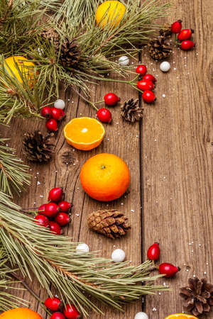 Spirit Christmas background. Fresh mandarins, dog-rose berries, candies, pine branches and cones, artificial snow. Nature decorations, vintage wooden boards, flat lay, copy space, close upの写真素材