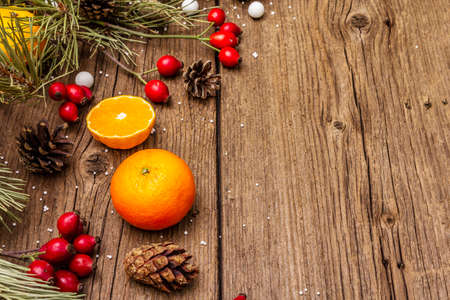 Spirit Christmas background. Fresh mandarins, dog-rose berries, candies, pine branches and cones, artificial snow. Nature decorations, vintage wooden boards, flat lay, copy spaceの写真素材