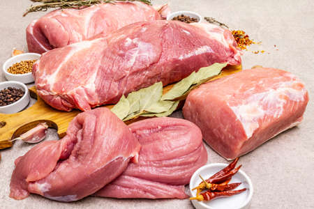 Assorted various fresh pork cuts. Raw meat with spices. Tenderloin, shoulder blade, neck, hind leg steak. Stone concrete background, close upの写真素材