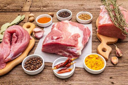 Assorted various fresh pork cuts. Raw meat with spices. Tenderloin, shoulder blade, neck. Old wooden boards background, close upの写真素材