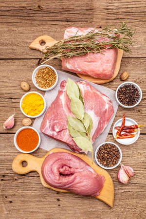 Assorted various fresh pork cuts. Raw meat with spices. Tenderloin, shoulder blade, neck. Old wooden boards background, top viewの写真素材