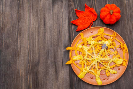Spider web pancakes with sugar syrup and powder for Halloween breakfast. With crochet orange pumpkin and leaf. Dark wooden background, copy space, top viewの写真素材