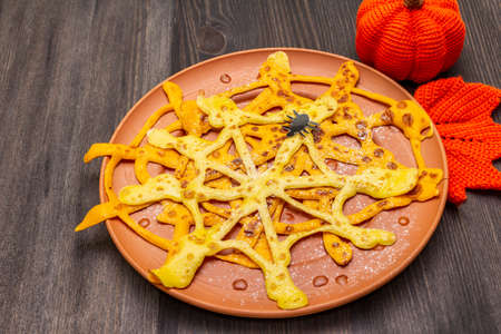 Spider web pancakes with sugar syrup and powder for Halloween breakfast. With crochet orange pumpkin and leaf. Dark wooden background, close upの写真素材