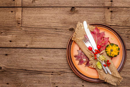 Autumn and Thanksgiving dinner place setting. Harvest of vegetables and berries, colorful leaves, hops, ceramic plates, fork and knife, napkin. Fall cutlery wooden background, copy space, top viewの写真素材