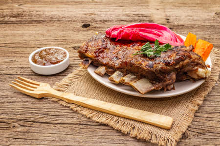 BBQ pork ribs with fermented cabbage, baked carrot, fresh parsley. Teriyaki sauce, spices, plum chutney. Old wooden boards background, close upの写真素材