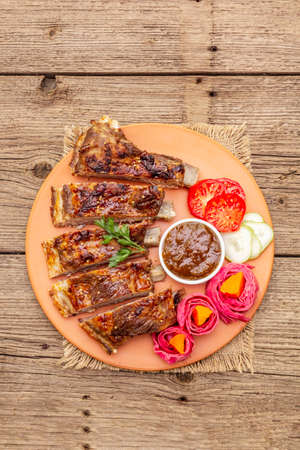 BBQ pork ribs with fermented, baked and fresh vegetables. Teriyaki sauce, spices, plum chutney. Old wooden boards background, copy space, top viewの写真素材