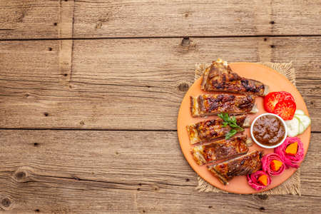 BBQ pork ribs with fermented, baked and fresh vegetables. Teriyaki sauce, spices, plum chutney. Old wooden boards background, copy space, top viewの写真素材