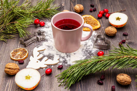 Christmas hot tea background. New Year mood, evergreen pine, nuts, berries, apples, orange. Cookie cutters, flour, deer. Wooden boardsの写真素材
