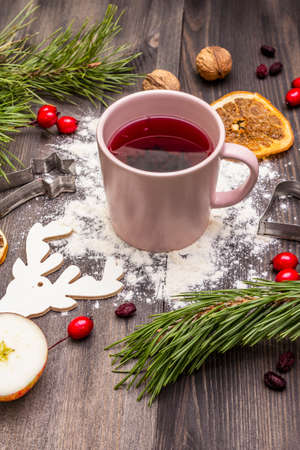 Christmas hot tea background. New Year mood, evergreen pine, nuts, berries, apples, orange. Cookie cutters, flour, deer. Wooden boardsの写真素材