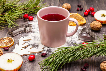 Christmas hot tea background. New Year mood, evergreen pine, nuts, berries, apples, orange. Cookie cutters, flour, deer. Wooden boards, close upの写真素材