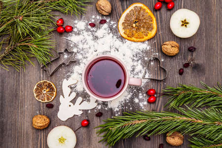 Christmas hot tea background. New Year mood, evergreen pine, nuts, berries, apples, orange. Cookie cutters, flour, deer. Wooden boards, top viewの写真素材
