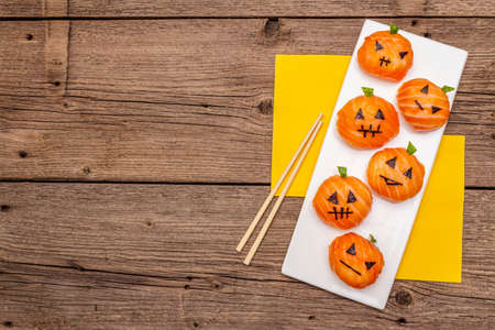 Funny Halloween Sushi Pumpkins Jack o Lantern, Sushi Monsters. Temari sushi, sushi balls. Healthy food for kids. Napkins, chopsticks, old wooden boards background, top view, copy spaceの写真素材