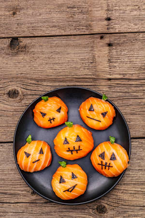 Funny Halloween Sushi Pumpkins Jack o Lantern, Sushi Monsters. Temari sushi, sushi balls. Healthy food for kids. Black ceramic plate, old wooden boards background, copy space, top view, close upの写真素材