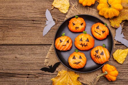 Funny Halloween Sushi Pumpkins Jack o Lantern, Sushi Monsters. Temari sushi, sushi balls. Healthy food for kids. Autumn leaves, bats, old wooden boards background, copy space, top viewの写真素材