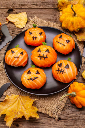 Funny Halloween Sushi Pumpkins Jack o Lantern, Sushi Monsters. Temari sushi, sushi balls. Healthy food for kids. Autumn leaves, bats, old wooden boards background, close upの写真素材
