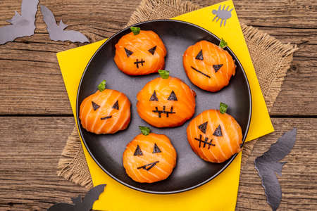 Funny Halloween Sushi Pumpkins Jack o Lantern, Sushi Monsters. Temari sushi, sushi balls. Healthy food for kids. Bats, napkins, old wooden boards background, top view, close upの写真素材