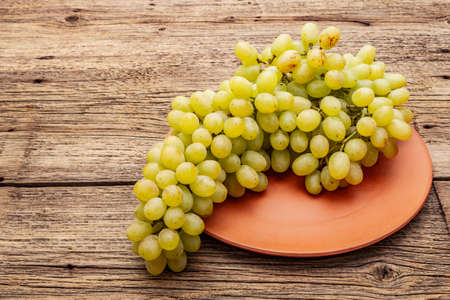 Bunch of sweet green seedless grapes variety "Kishmish". Ripe fruits autumn harvest. Healthy food concept. Old wooden boards background, ceramic plate, copy space, close upの写真素材