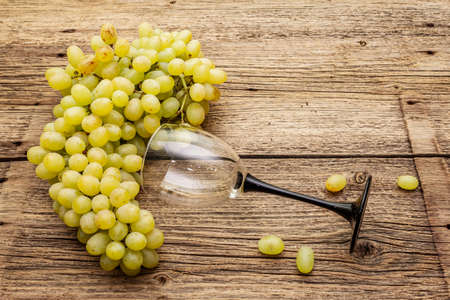 Bunch of sweet green seedless grapes variety "Kishmish". Ripe fruits autumn harvest. Healthy food concept. Old wooden boards background, wine glass, copy space, close upの写真素材